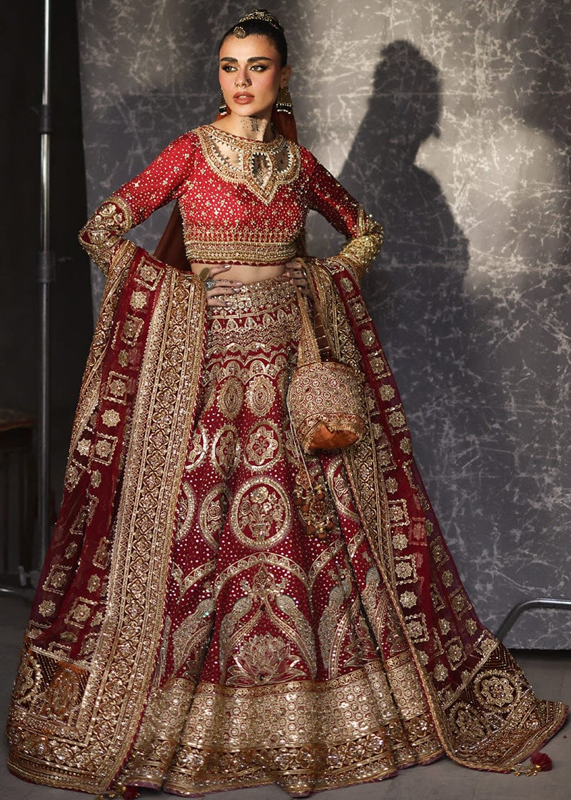 Woman in a traditional red and gold embroidered outfit against a textured gray background Malika Jann by MNR
